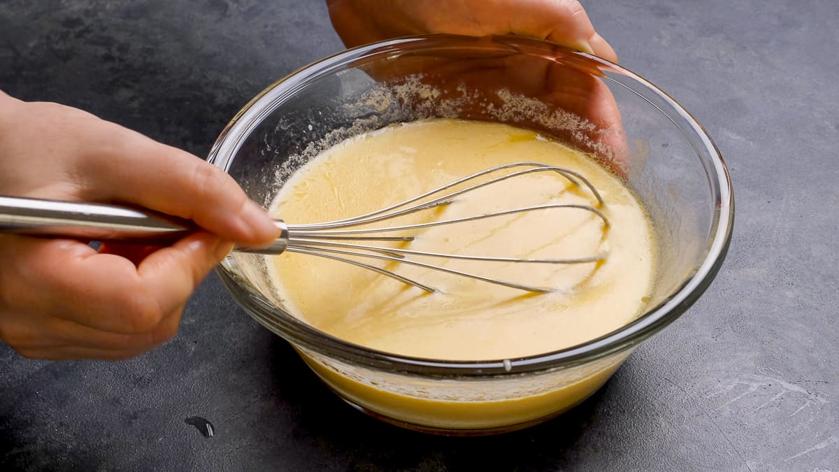 Hands whisking yogurt and eggs in a bowl.