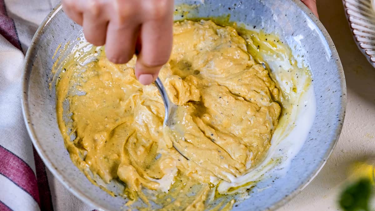 Hand mashing egg yolks and other ingredients with a fork in a bowl.