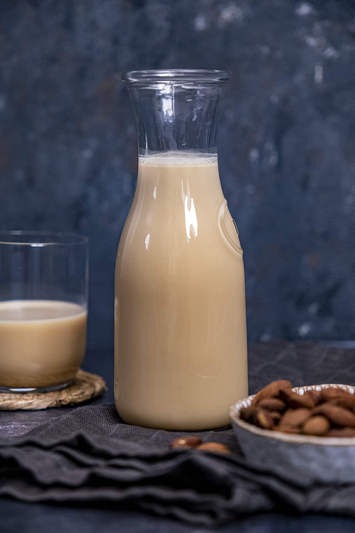 Roasted almond milk in a bottle and in a glass and whole almonds on the side on a background.