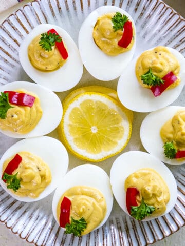 Deviled eggs garnished with sweet peppers and parsley on a white plate.