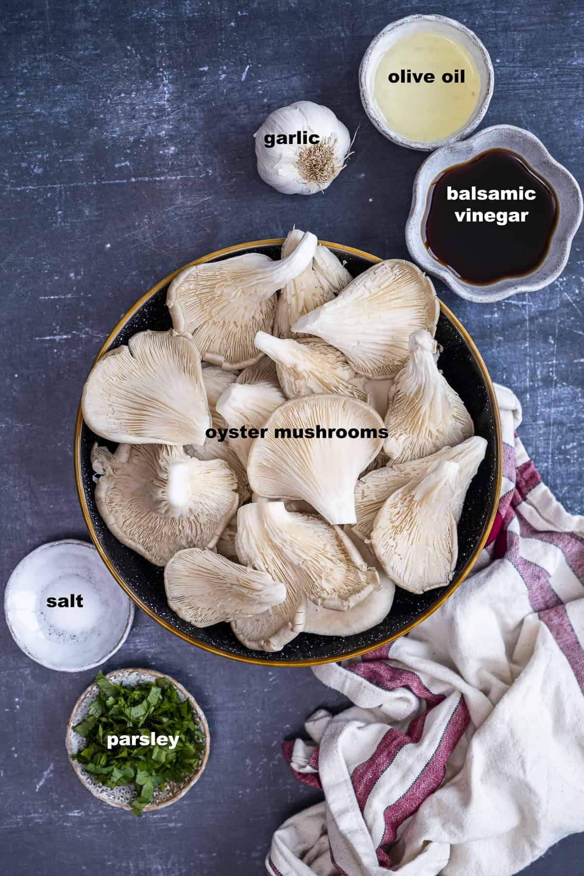 Oyster mushrooms, garlic, oil, balsamic vinegar, salt and parsley in separate bowls on a dark background.