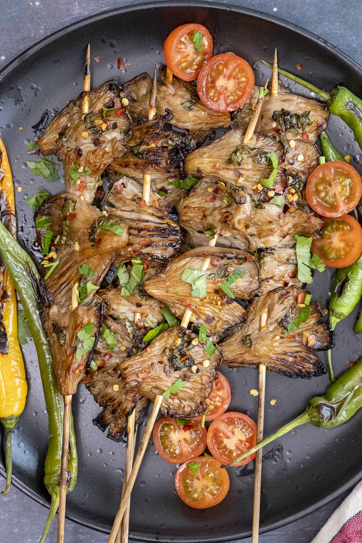 Grilled oyster mushroom skewers, peppers and tomatoes on a black plate.