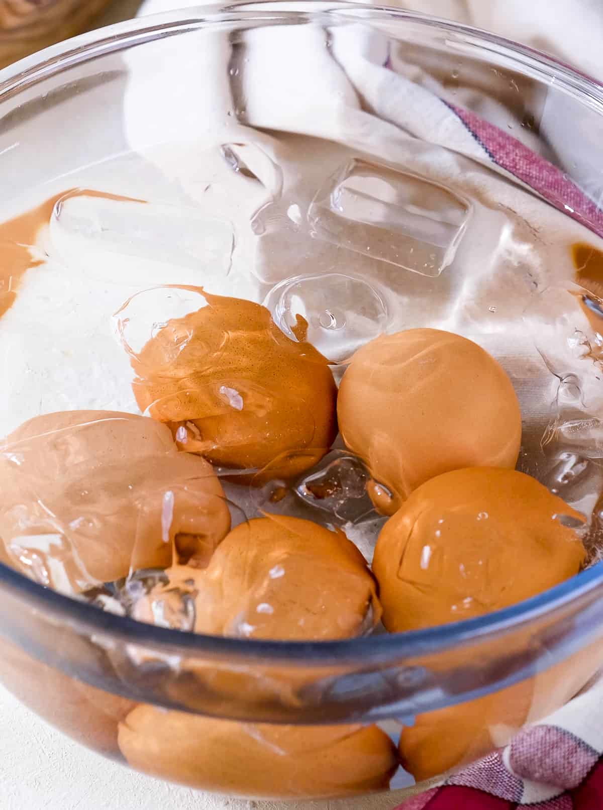 Cooked eggs in a glass bowl with col water.