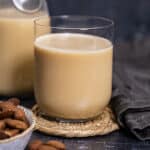 Almond milk from roasted almonds in a glass, a bottle on the back and whole almonds on the side.