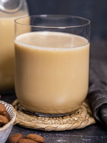 Almond milk from roasted almonds in a glass, a bottle on the back and whole almonds on the side.