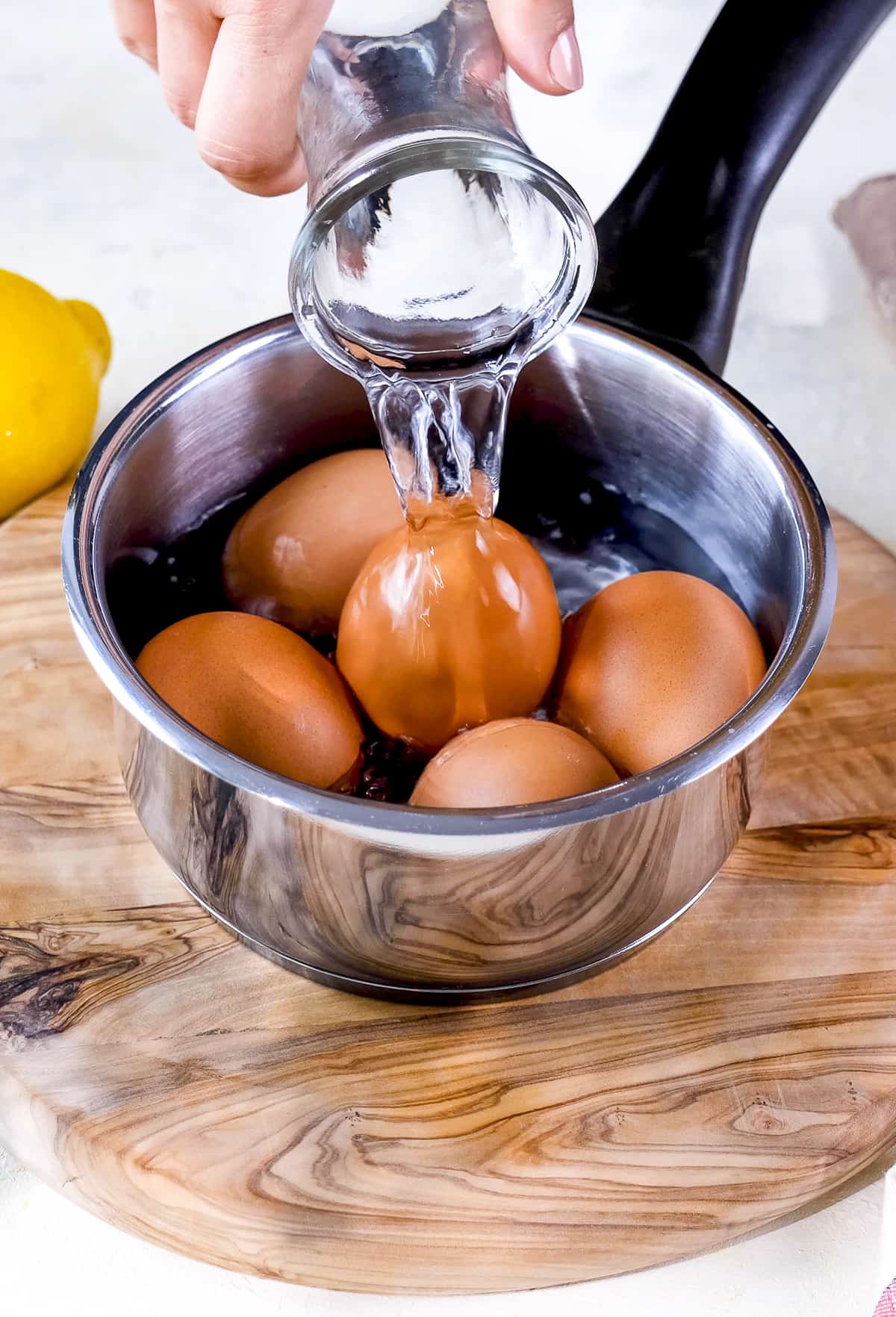 Hand pouring water over the eggs in a saucepan.