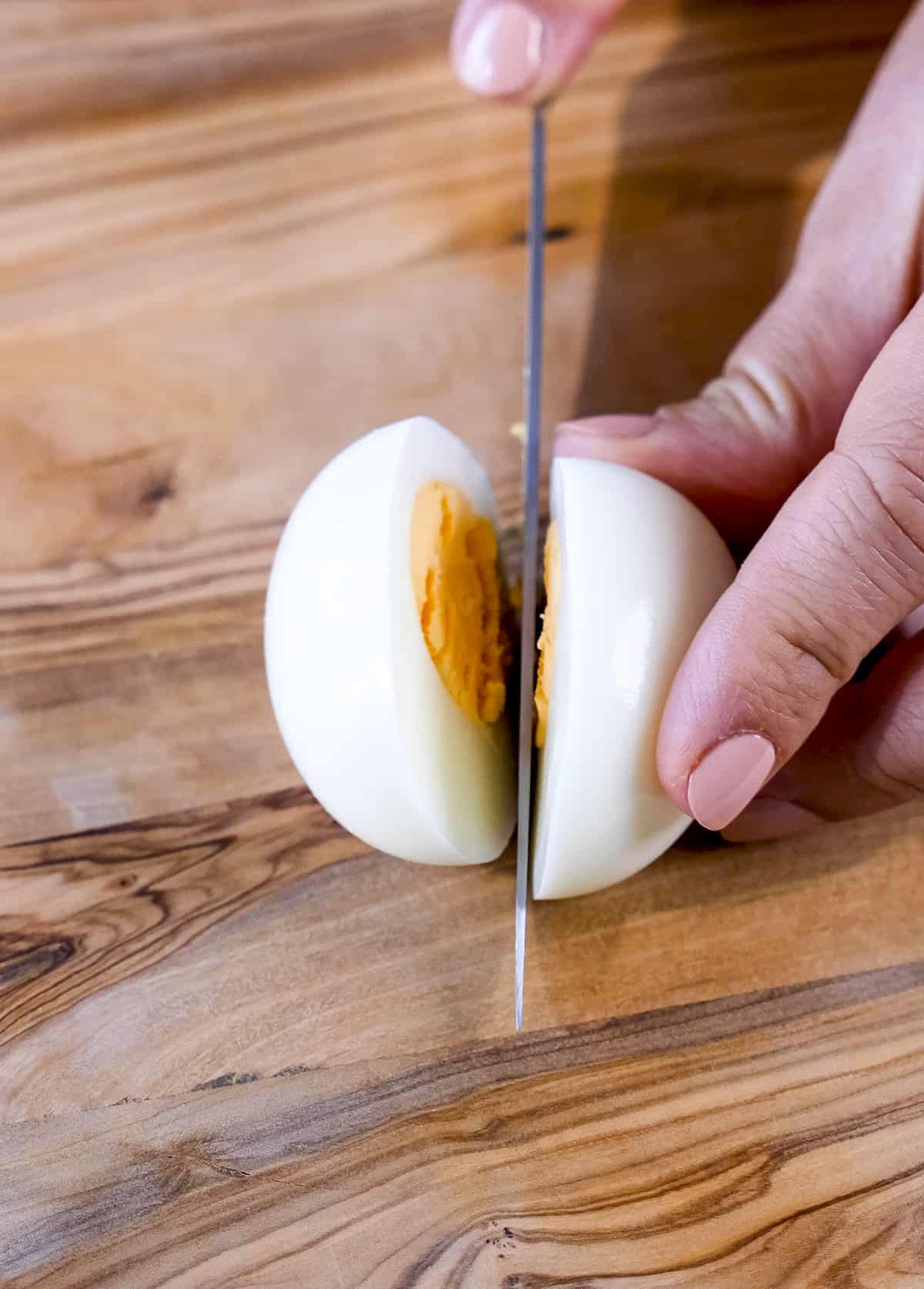 Hands cutting a hard boiled egg with a knife.