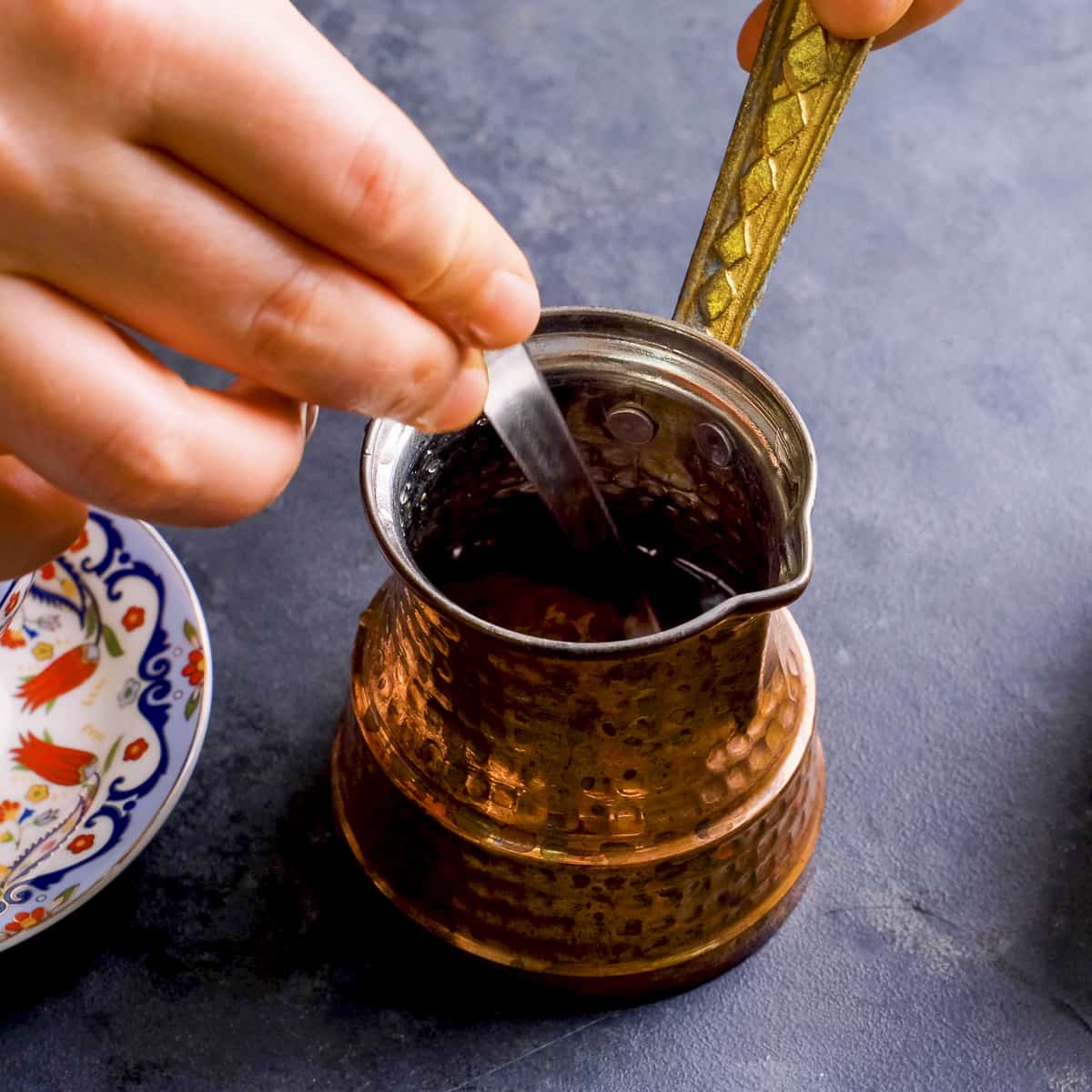 A hand mixing coffee and water in a traditional pot with.