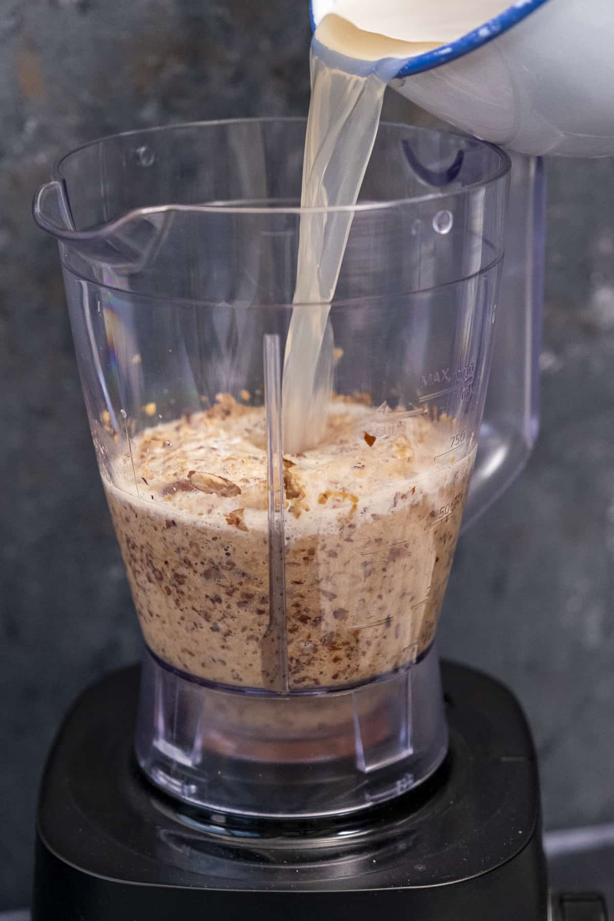 Water being poured over blended almonds in a blender.