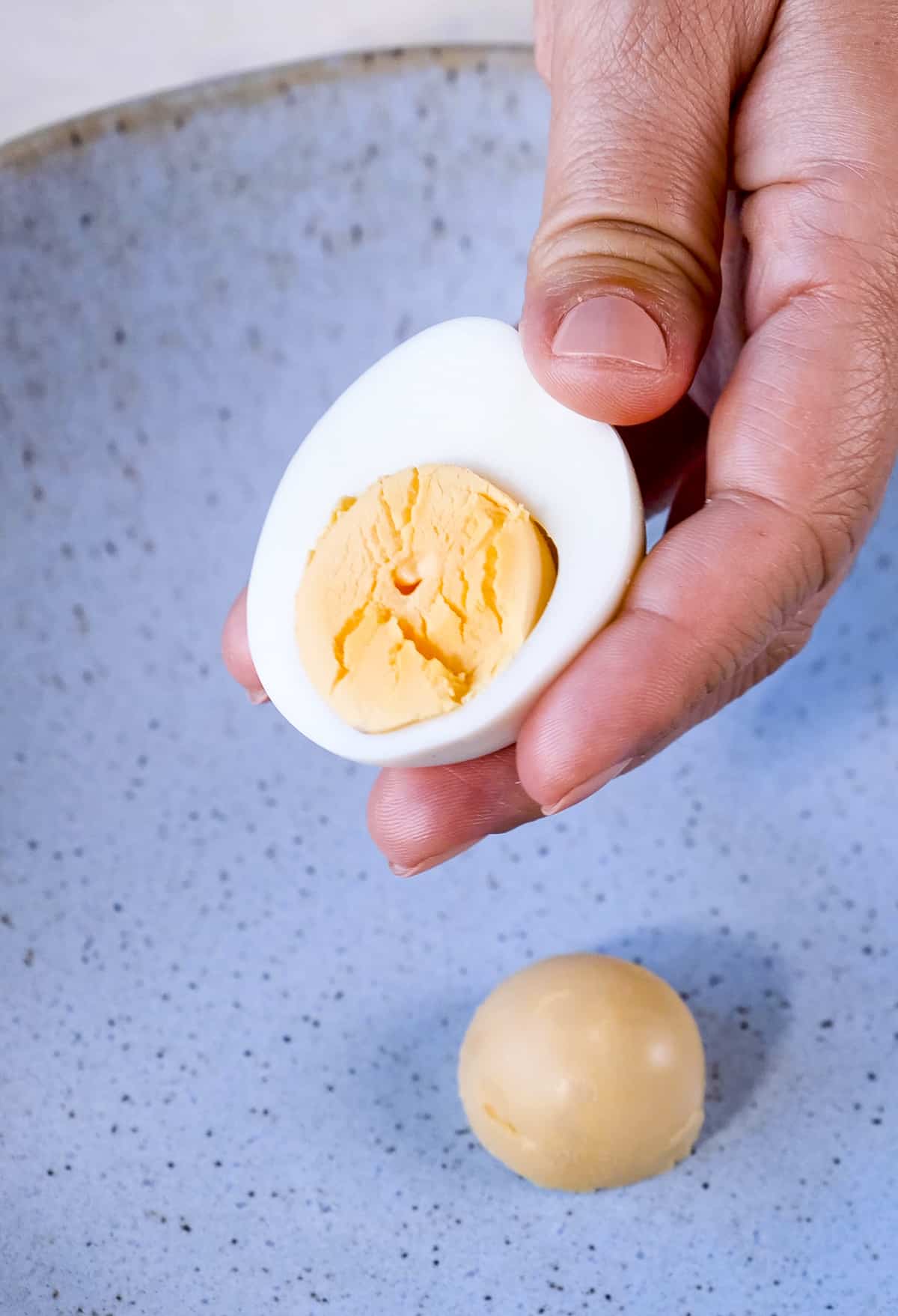 Hand gently squeezing half of a hard boiled egg to loosen the yolk.