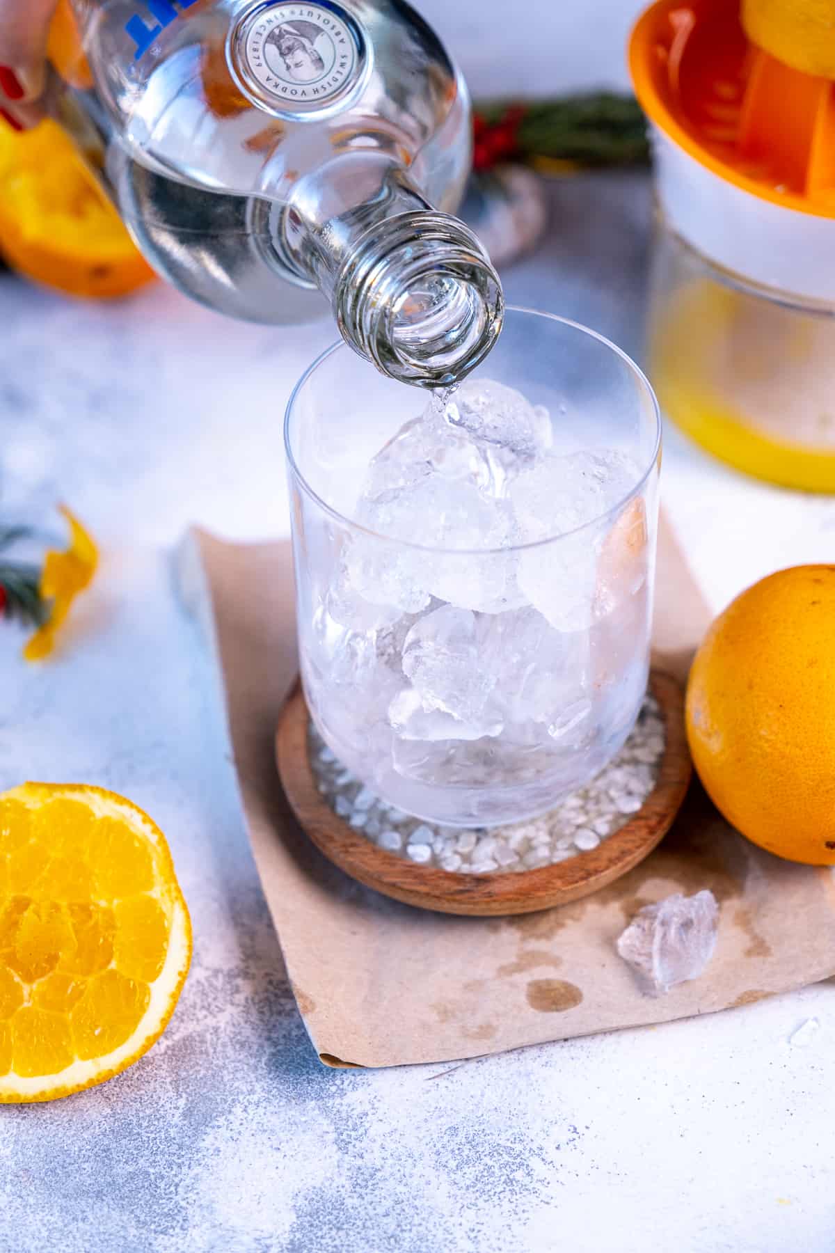 A hand pouring vodka from a bottle over ice in a glass.