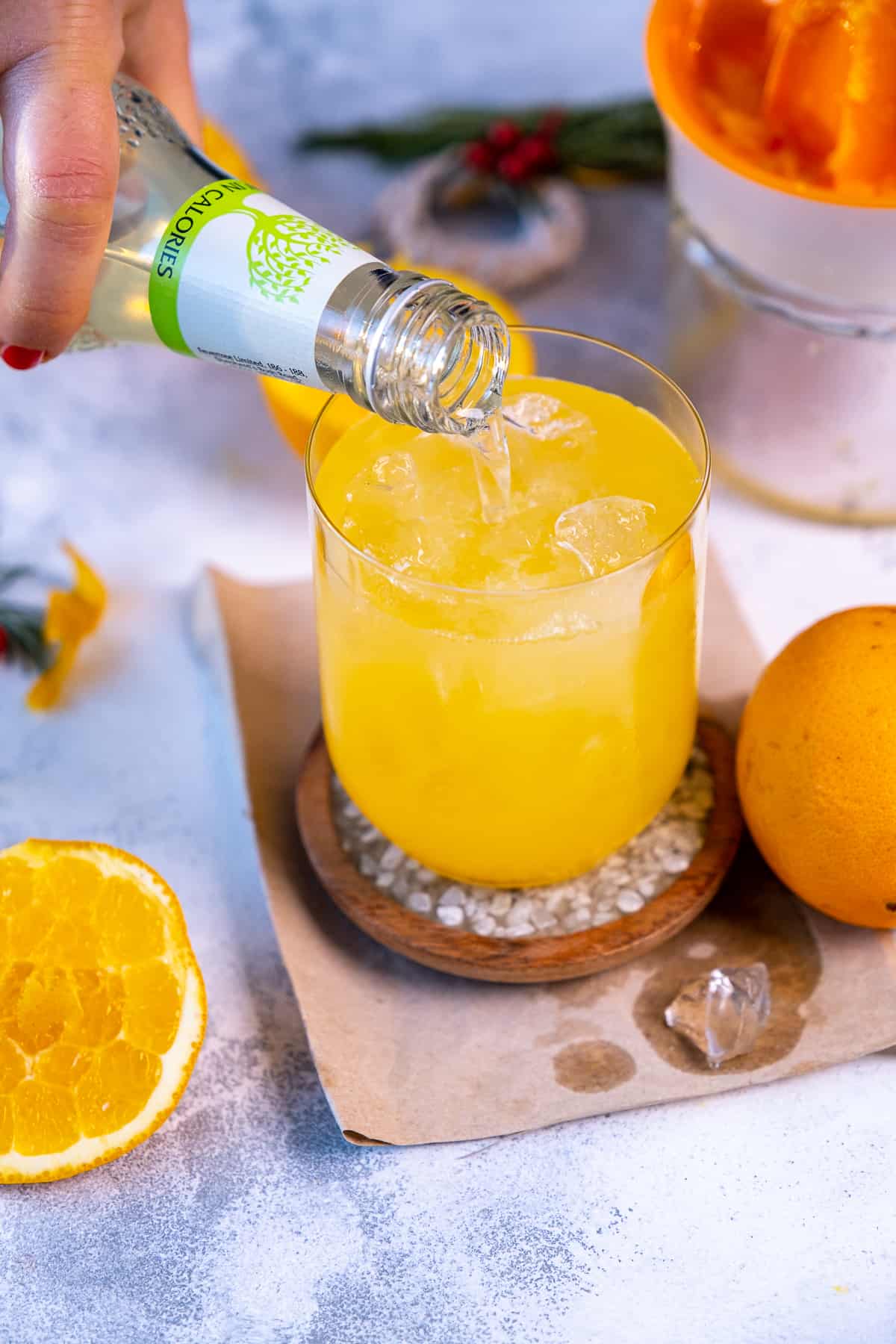 A hand pouring lime soda over vodka orange cocktail.
