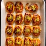 Golden brown Şekerpare cookies arranged in a white baking dish, topped with ground pistachios, with one broken to show the soft inside.