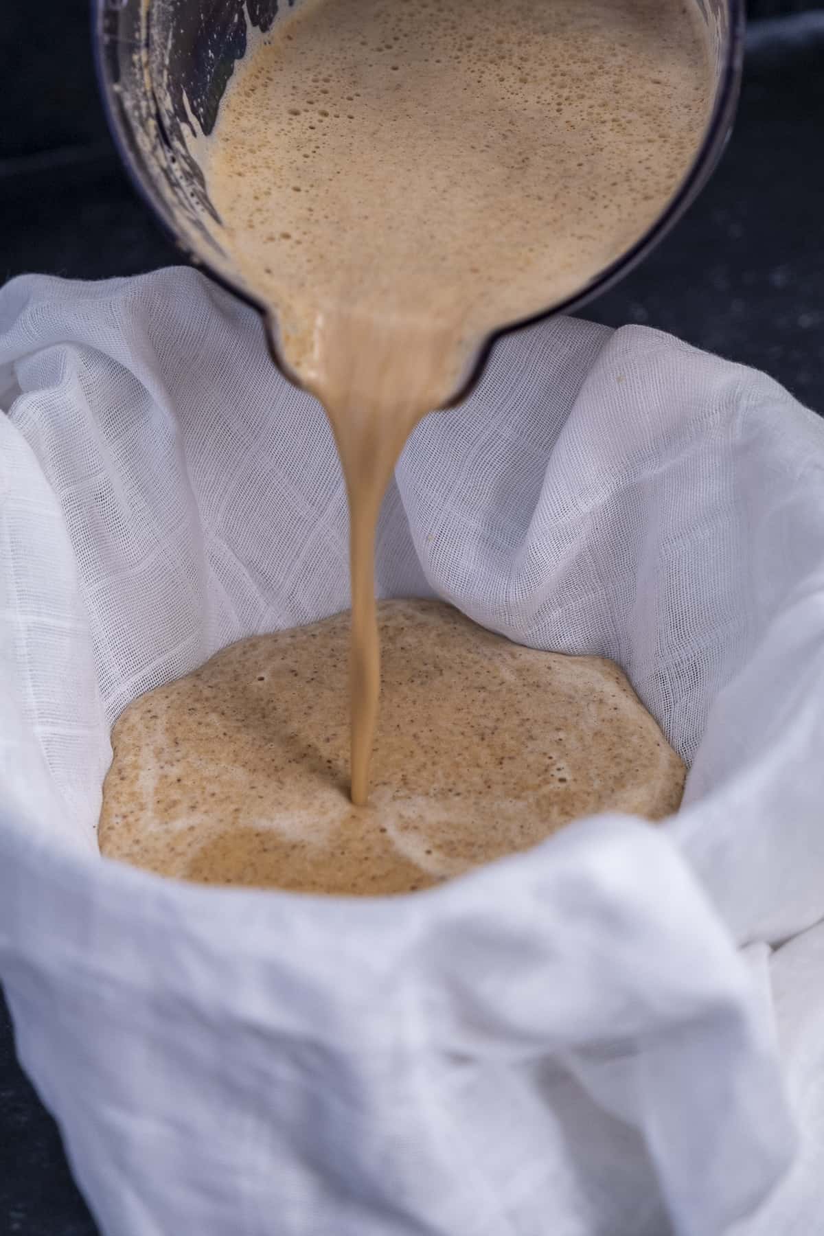 Blended almond milk is being poured into a white muslin.