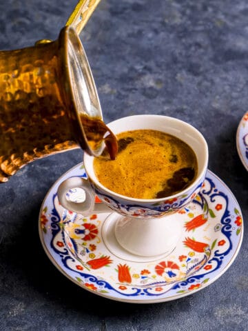 A copper Turkish coffee pot pouring coffee into a traditional cup.