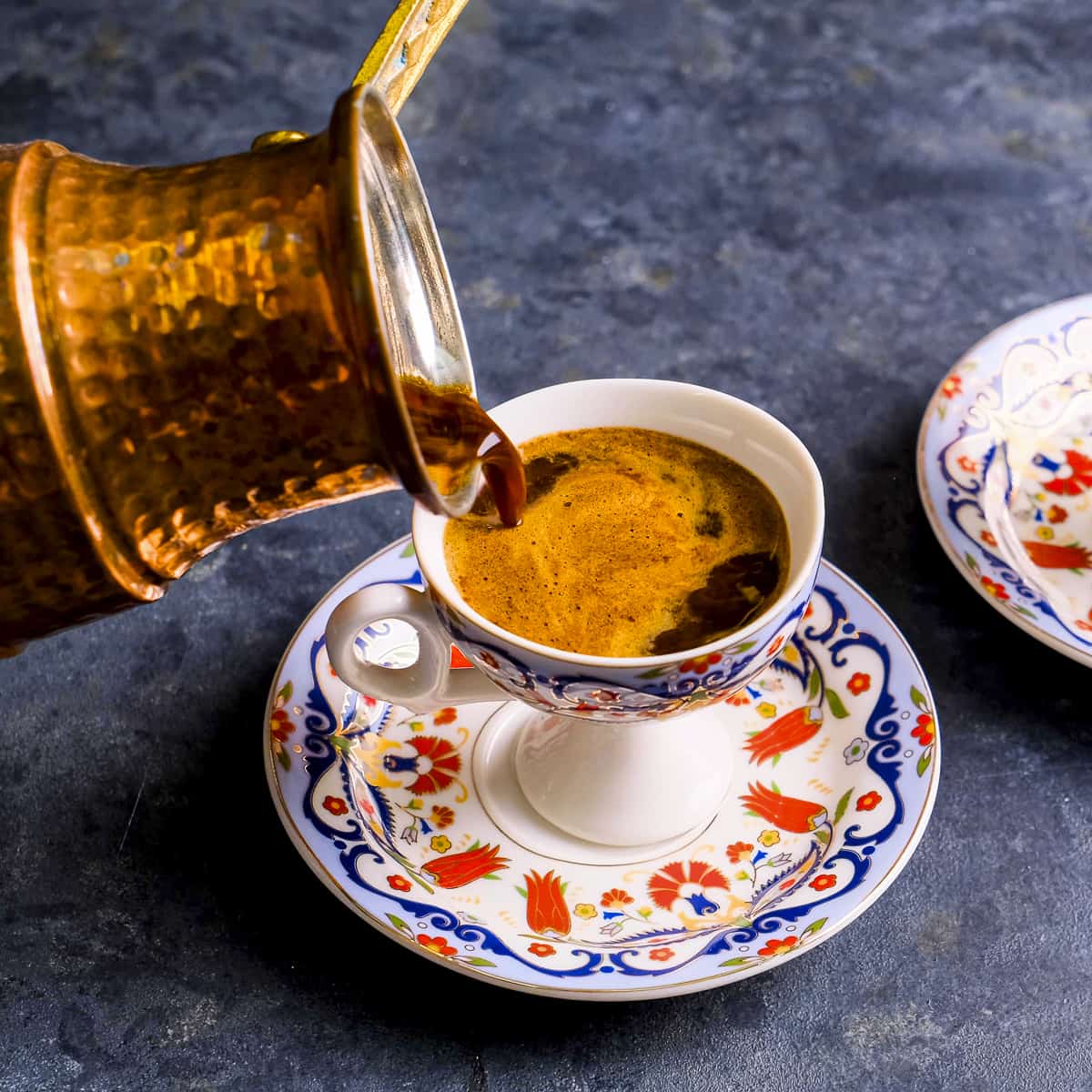 A copper Turkish coffee pot pouring coffee into a traditional cup.