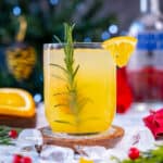 Orange vodka cocktail in a glass garnished with an orange slice and rosemary.