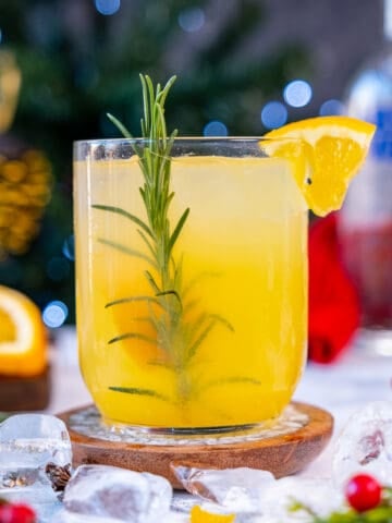 Orange vodka cocktail in a glass garnished with an orange slice and rosemary.