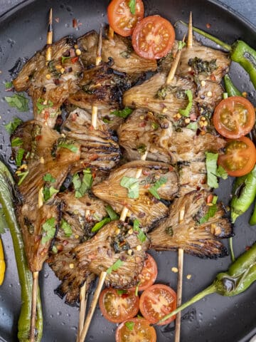 Grilled oyster mushrooms paired with grilled peppers and cherry tomatoes on a black plate.