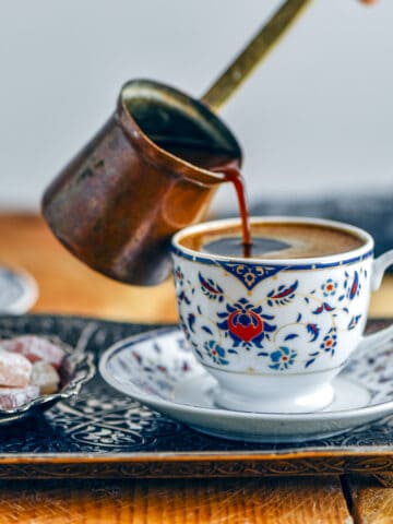 Pouring Turkish coffee from a copper pot into a traditional coffee cup.