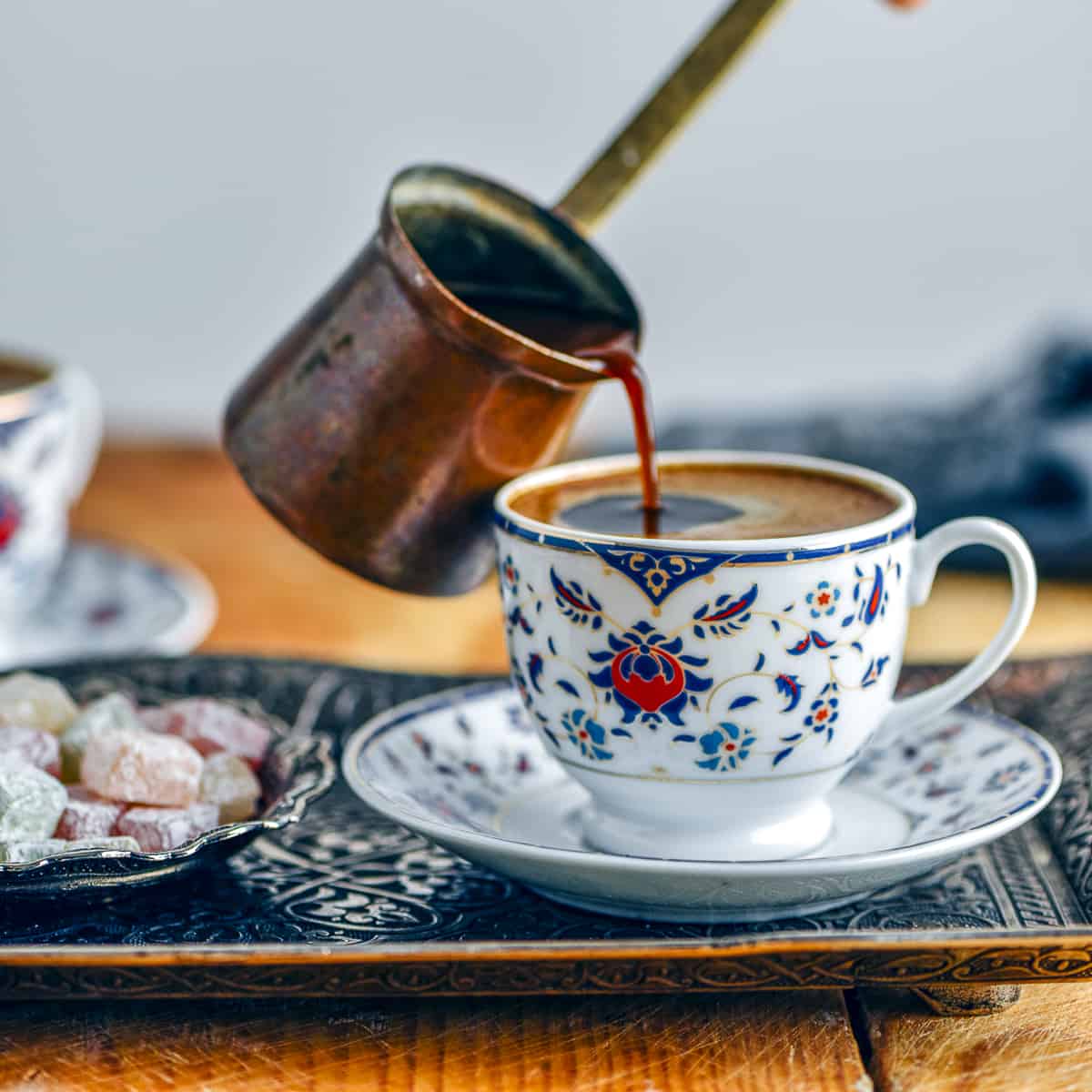 Pouring Turkish coffee from a copper pot into a traditional coffee cup.