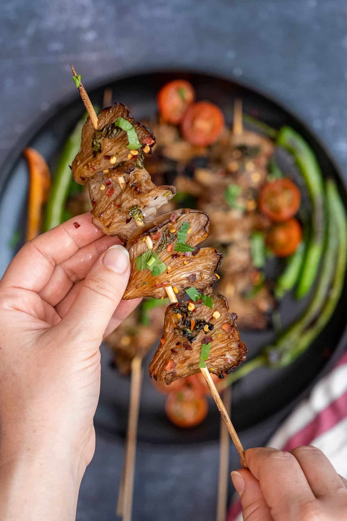 Hands holding a grilled mushroom skewer.