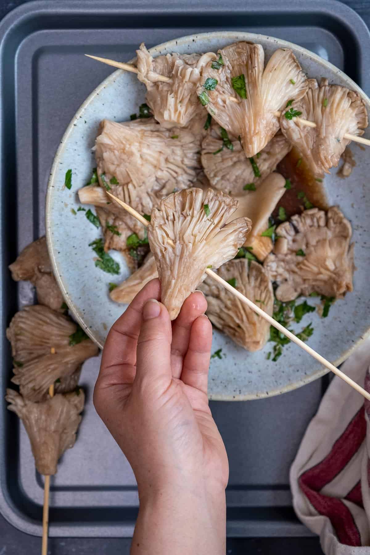 Hands threading marinated oyster mushrooms on wooden skewers.
