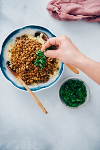 Woman garnishing vegan bolognese sauce with chopped parsley.