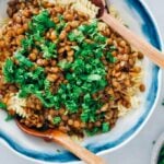 Vegan bolognese garnished with fresh parsley in a white bowl with two wooden spoons.