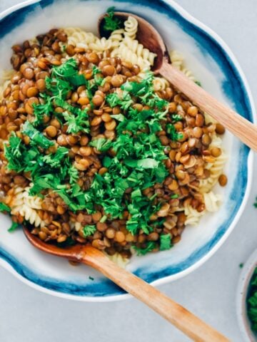 Vegan bolognese garnished with fresh parsley in a white bowl with two wooden spoons.