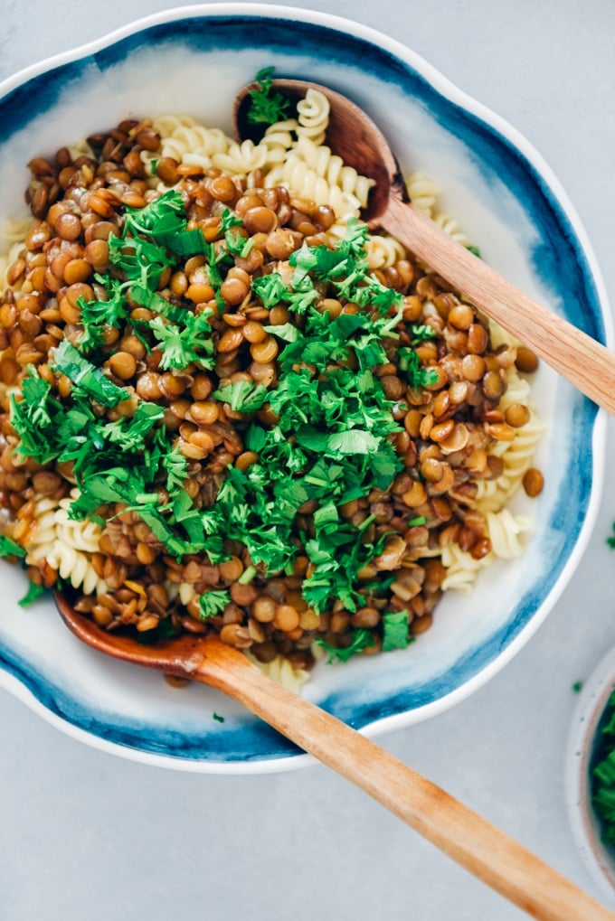 Vegan bolognese garnished with fresh parsley in a white bowl with two wooden spoons.