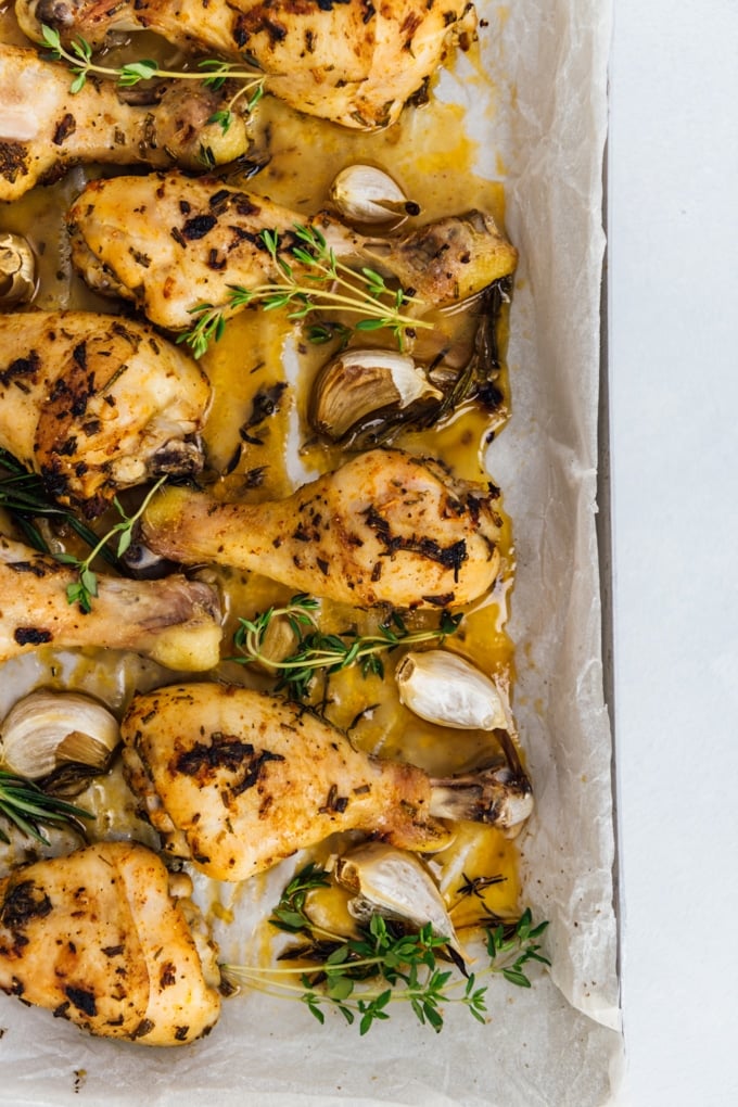 Oven baked chicken drumsticks with garlic cloves, rosemary and fresh thyme in a baking sheet