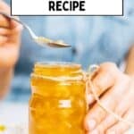 Hand holding a jar of homemade lemon jam with a spoon scooping from the top.