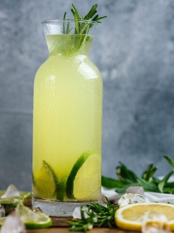 Vodka lemonade flavored with rosemary in a bottle garnished with lime slices.