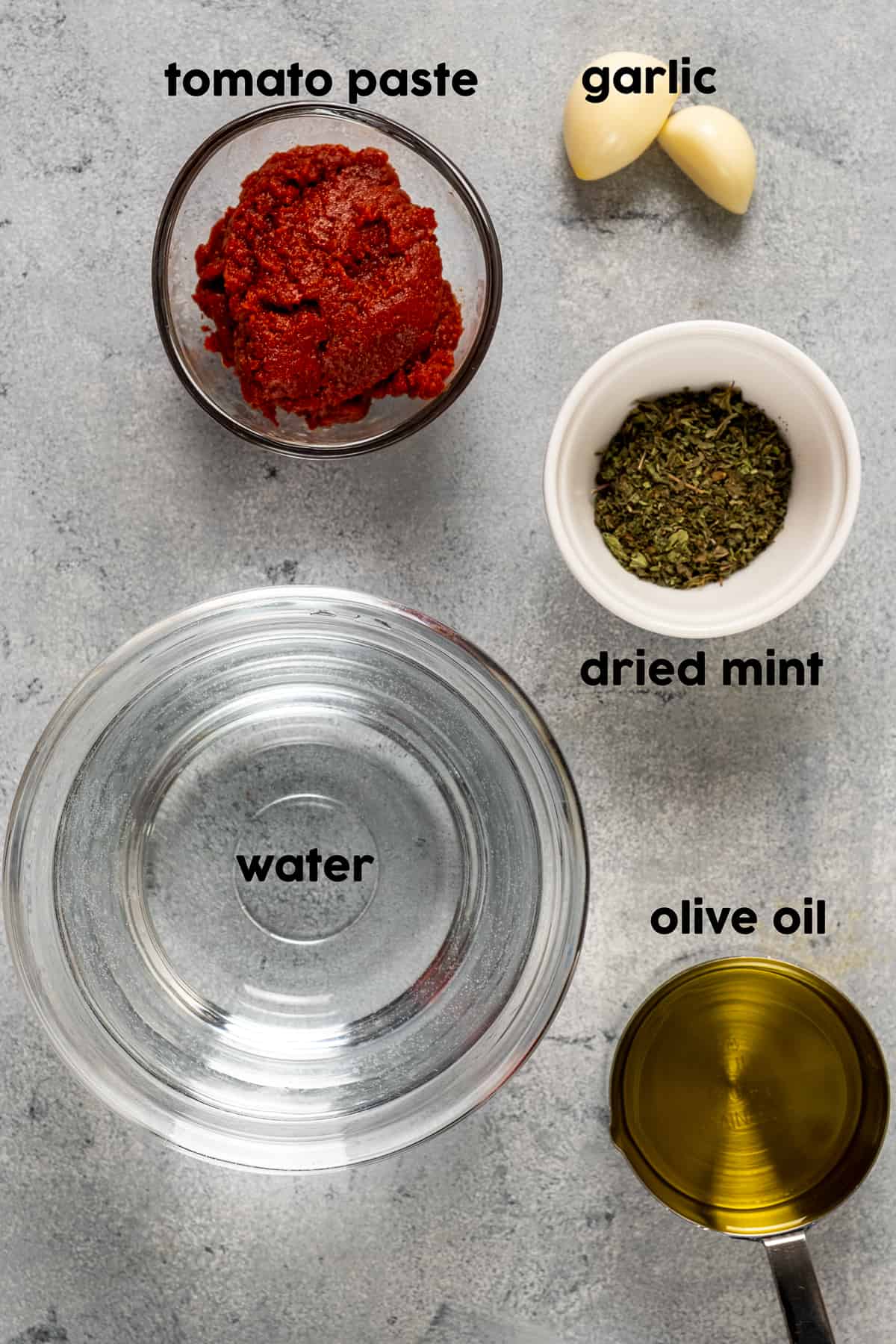 Water, tomato paste, dried mint, garlic and olive oil photographed on a light background.