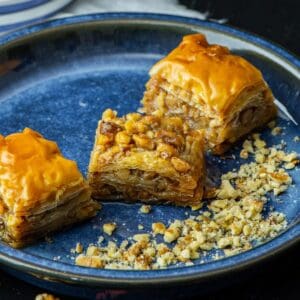 Turkish walnut baklava pieces with syrup glaze and crushed walnuts on a blue plate.