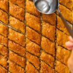 Turkish baklava in tray with syrup being poured over pieces.