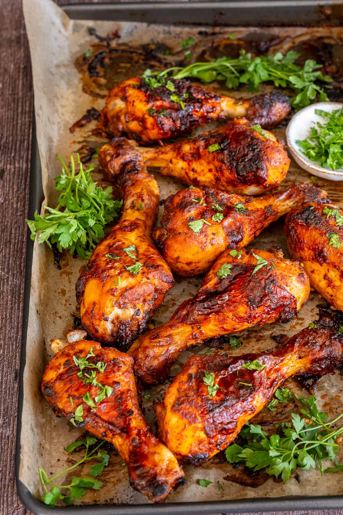 Oven-roasted Turkish chicken legs on a baking tray, topped with chopped parsley and served with fresh herbs.