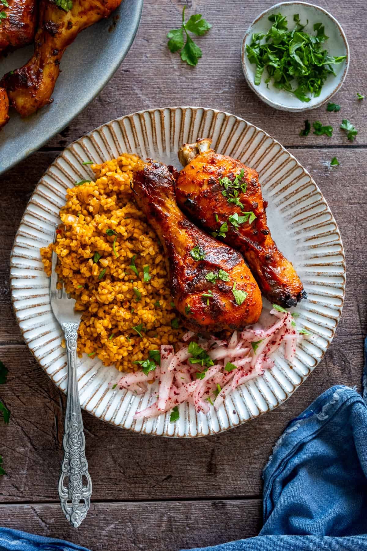 Plate of Turkish chicken legs served with bulgur pilaf and sumac onions, garnished with fresh parsley.