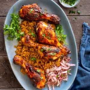 Oven-baked Turkish chicken legs served on bulgur pilaf with sumac onions and fresh parsley on a blue plate.