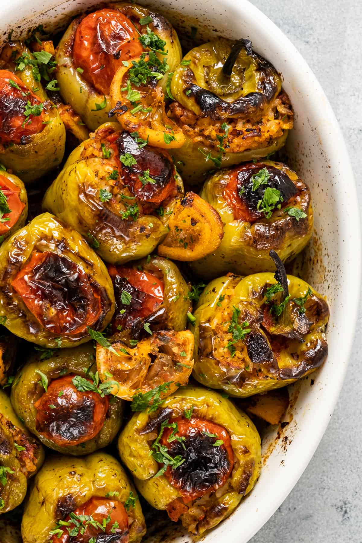 Rice stuffed green peppers topped with tomatoes, lemon slices and chopped parsley in a baking pan.