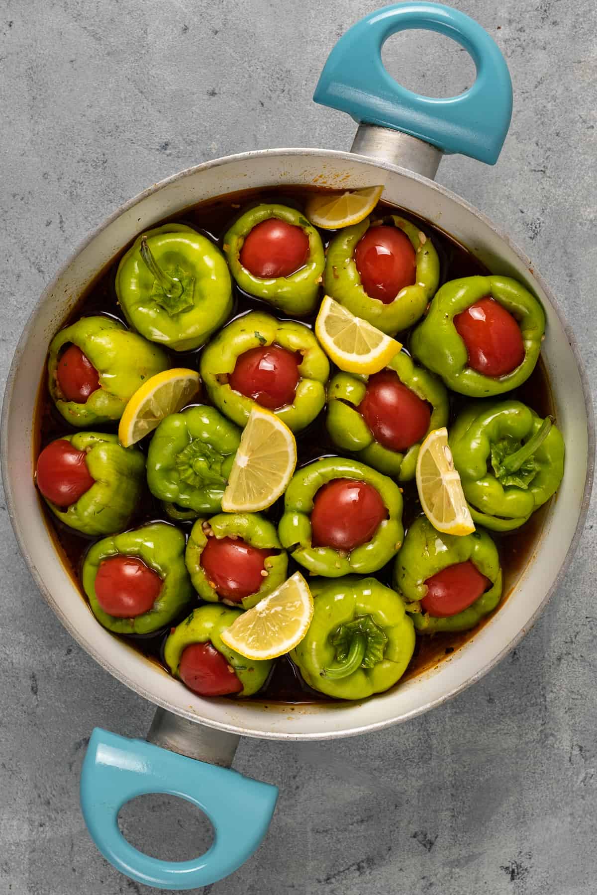 Turkish green peppers stuffed with a rice filling, topped with halved cherry tomatoes and garnished with lemon slices in a pan.