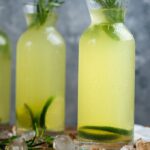 Vodka and lemonade together in bottles garnished with lime slices and rosemary.
