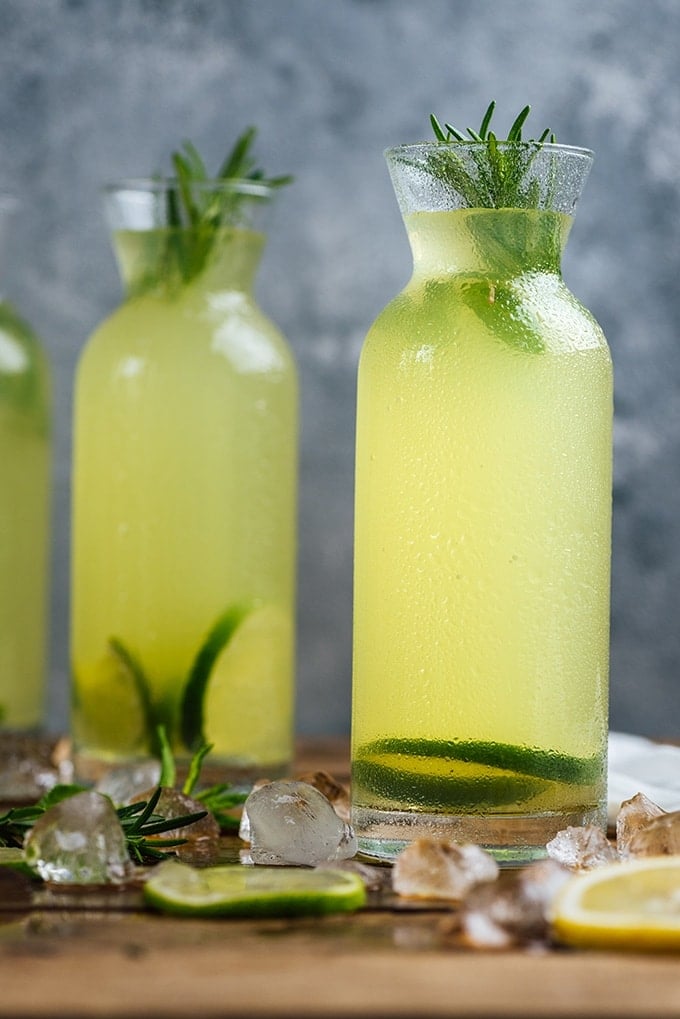 Vodka and lemonade together in bottles garnished with lime slices and rosemary.