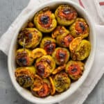 Baked rice stuffed green peppers in a white oval baking pan.