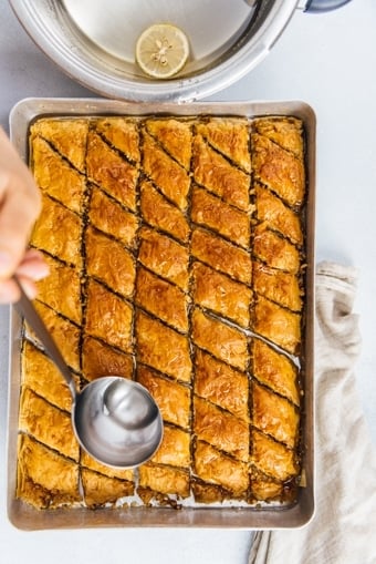 Pouring baklava syrup with a ladle over newly baked baklava