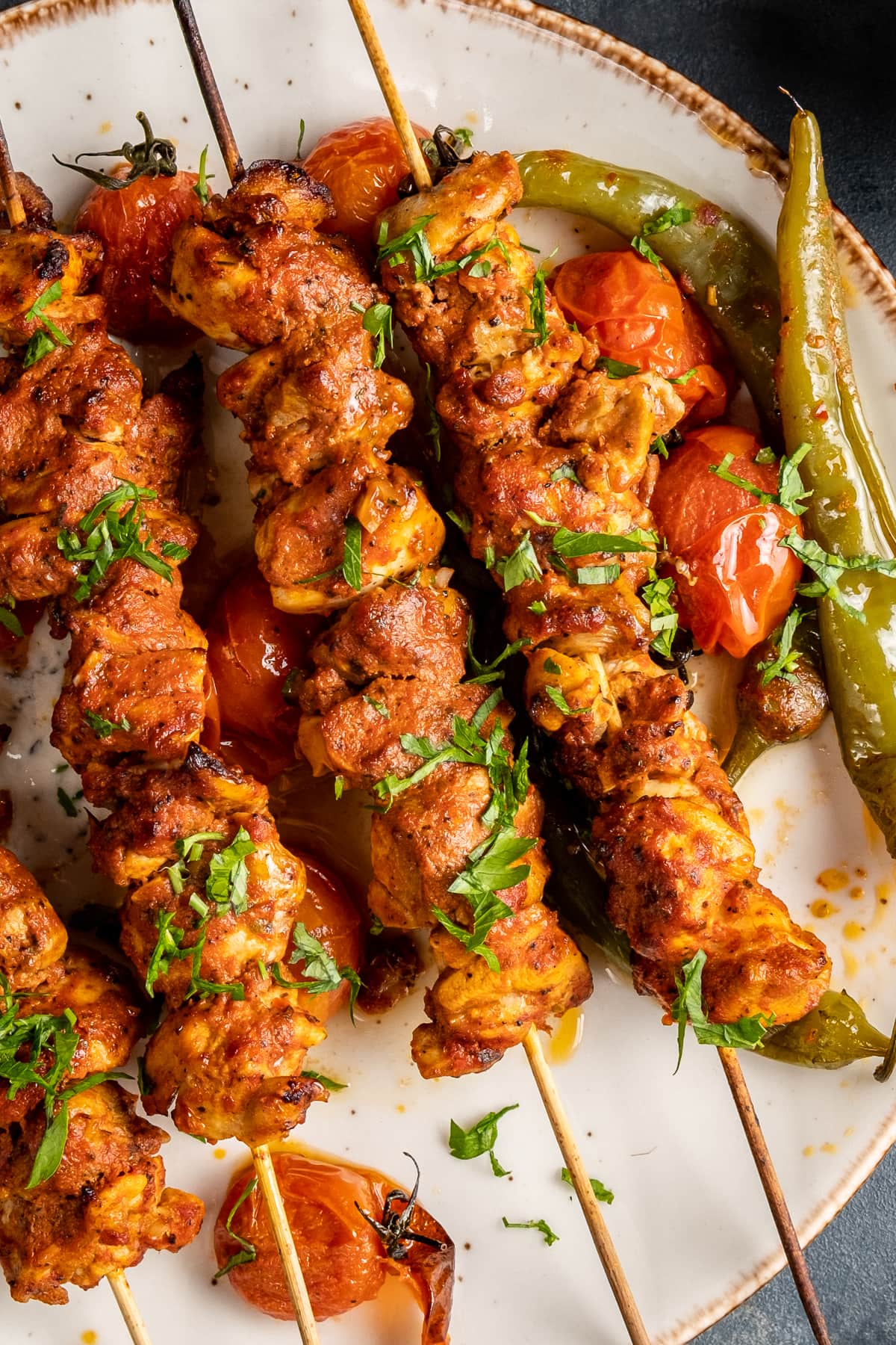 Chicken kabobs served with roasted tomatoes and peppers on a white plate.