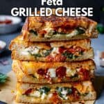 A stack of grilled cheese sandwiches stuffed with spinach and sun-dried tomatoes.