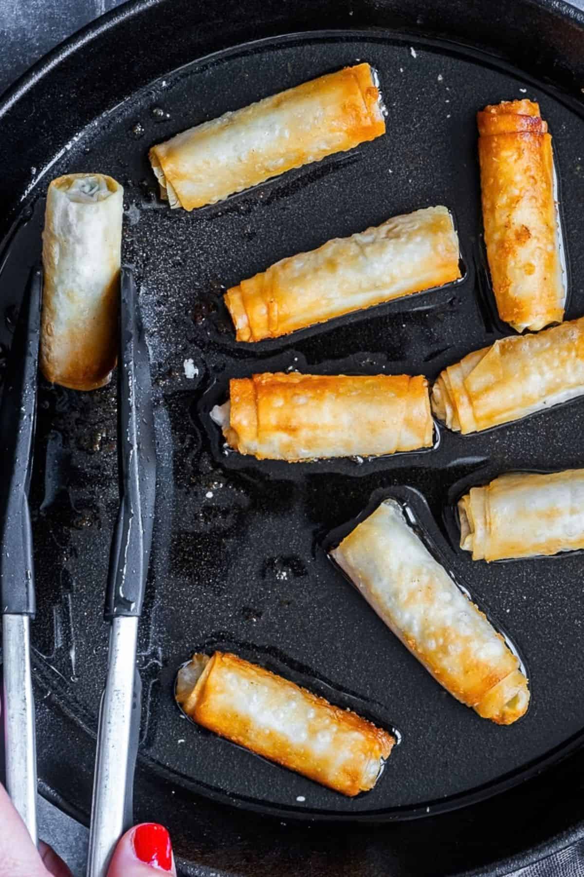 Sigara boregi rolls frying in oil in a pan, turning golden and crispy.