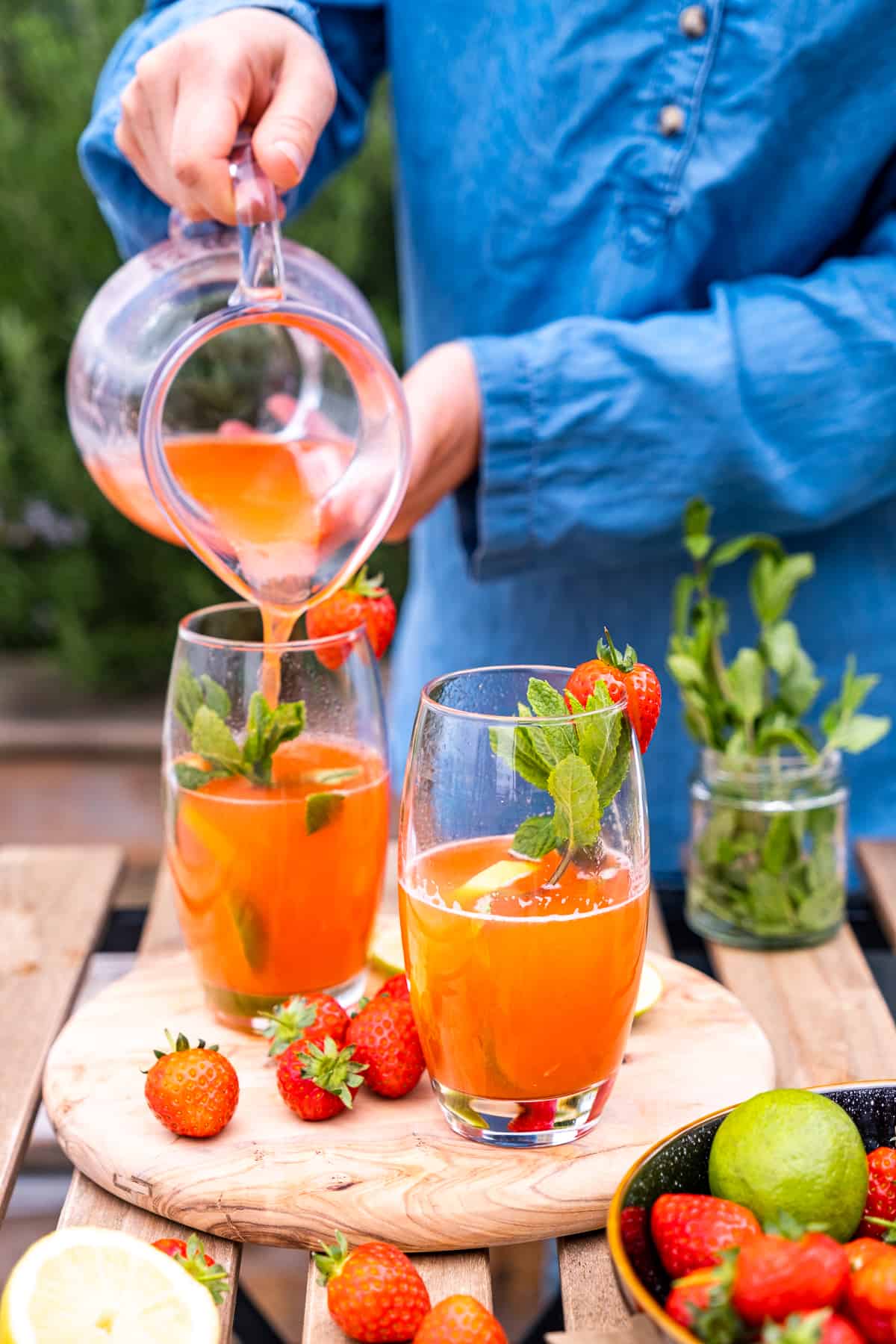 Woman pouring strawberry lemonade into tall glasses from a pitcher.